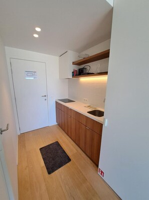 A compact kitchen with wooden cabinets, a white countertop, a sink, and a door with a sign. - Sea View Retreat for 2 in Oostduinkerke (Koksijde)