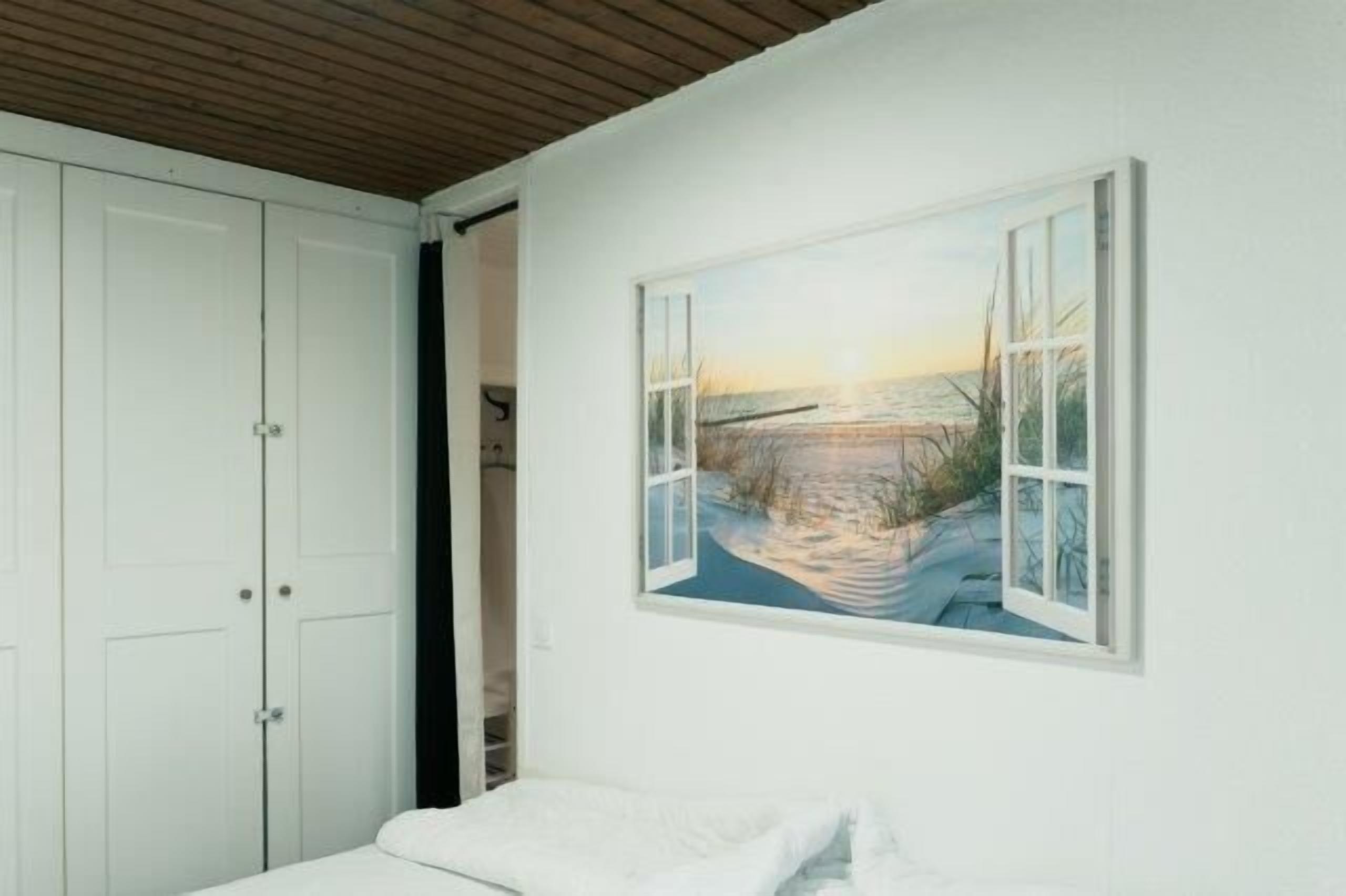 A bedroom with a bed, a white wardrobe, and a painting of a beach scene.