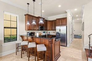 A kitchen with wooden cabinets, a stainless steel refrigerator, and a bar area with stools. - Golf Course Home with 4 King Beds and a Golf Cart (Miramar Beach)