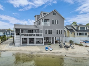Ein zweistöckiges Haus mit Balkon, Terrasse und Strandabschnitt mit Stand-Up-Paddleboards.