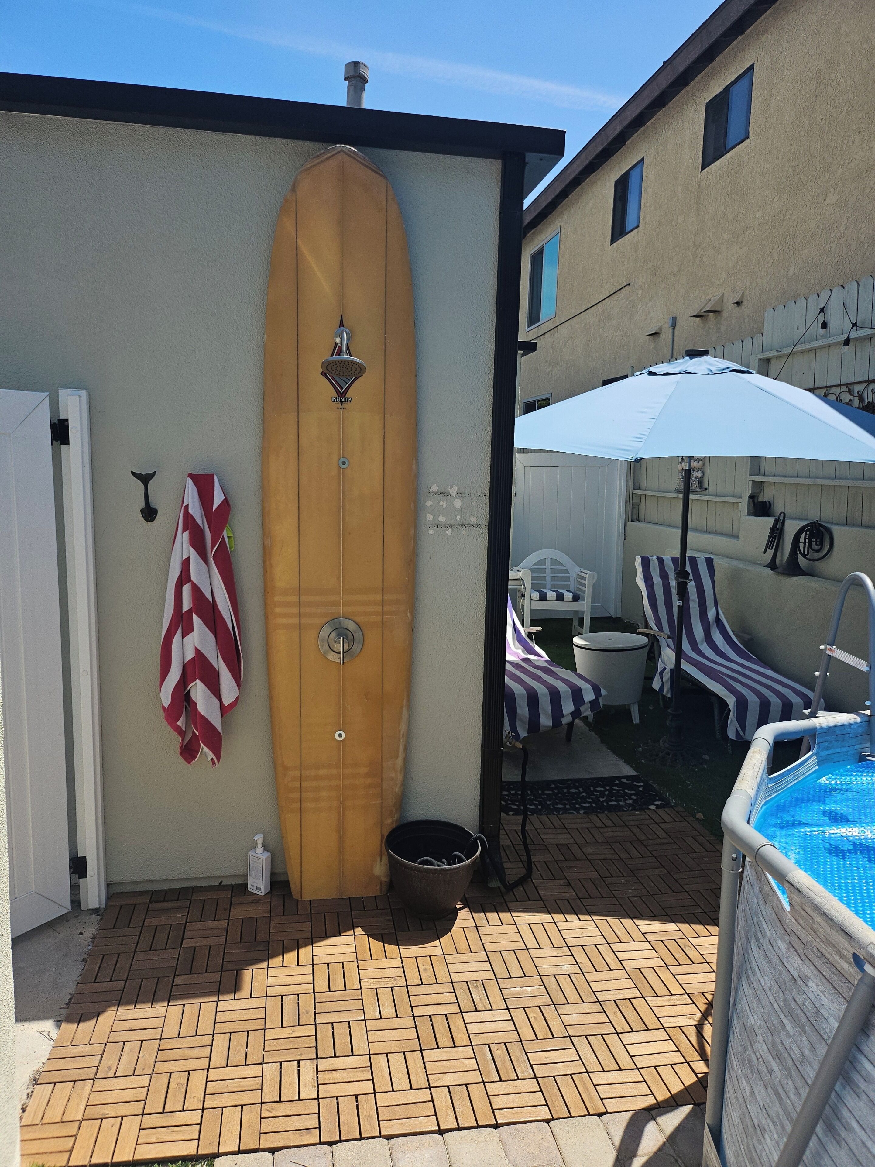 Ein Poolbereich mit einem Holzsurfboard, einem Eimer und einer weißen Tür.