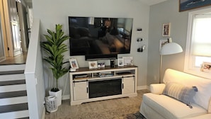 Uma sala de estar com televisão de tela plana, um sofá, uma mesa de centro e uma escada que leva a outro cômodo.