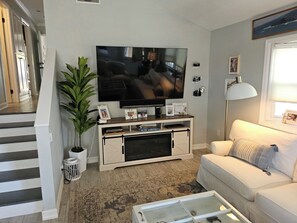 Una sala de estar con un televisor de pantalla plana, un sofá, una mesa de centro y una escalera que lleva a otra habitación.