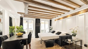Quarto moderno com cama, mesa de jantar com cadeiras, uma mesinha de apoio e uma janela grande com cortinas.