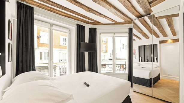 Quarto de hotel com uma cama grande, televisão de tela plana, espelho e varanda com vista para a cidade.