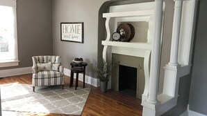 Uma sala de estar com lareira, uma poltrona listrada, um tapete e uma placa na parede.