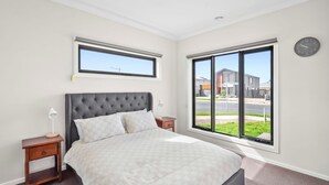 Un dormitorio con cama, mesitas de noche, una ventana con vistas y un reloj de pared.