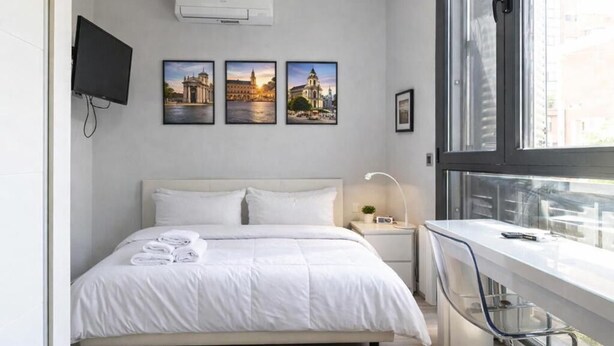 Una habitación de hotel moderna con cama, escritorio, televisor y tres cuadros en la pared.