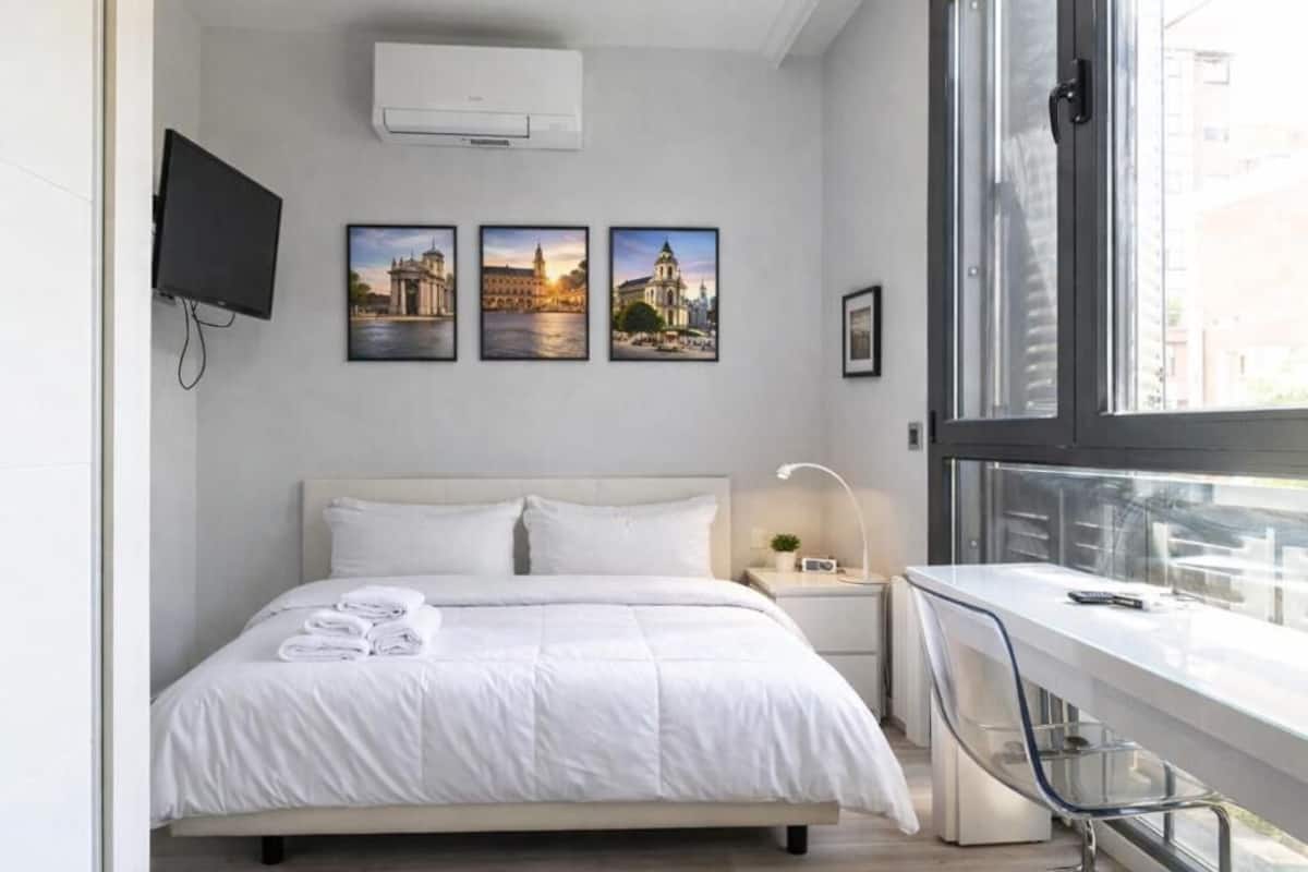Una habitación de hotel moderna con cama, escritorio, televisor y tres cuadros en la pared.