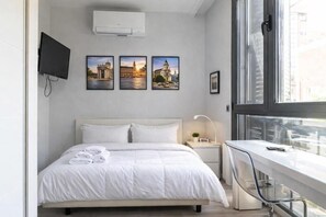A modern hotel room with a bed, a desk, a TV, and three framed pictures on the wall.
