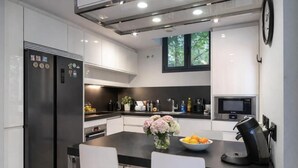 Una cocina moderna con encimera negra, armarios blancos, horno integrado, cafetera y ventana con vista a árboles.