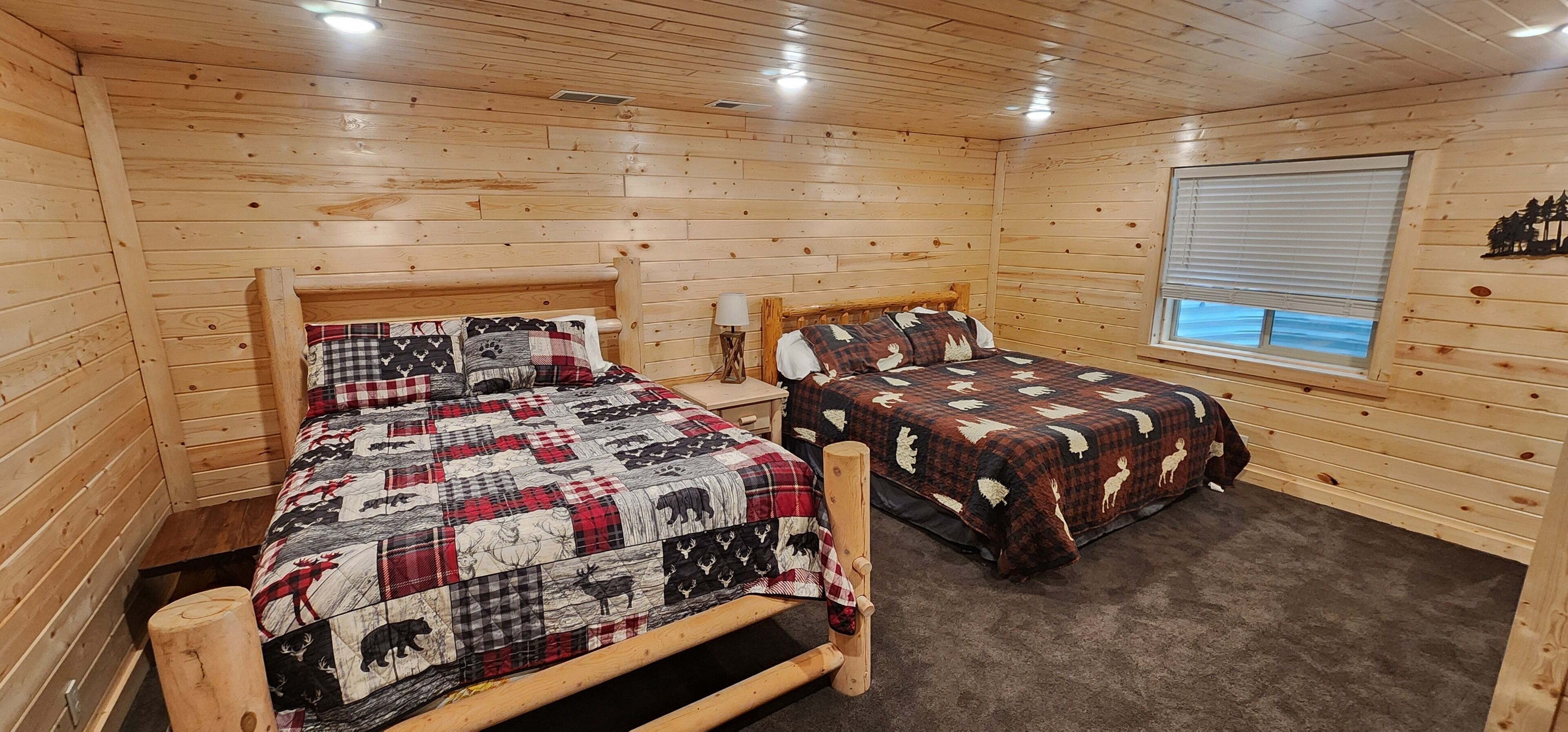 A cabin-style room with two wooden beds, a window with blinds, and a wooden ceiling.