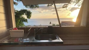 Cozinha com pia, escorredor de louça e janela com vista para o oceano ao pôr do sol.