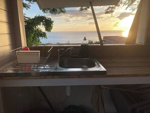 A kitchen with a sink, a dish rack, and a window overlooking the ocean at sunset. - Ayana Lodge - Sea view &clim Bouillante (Bouillante)