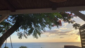 Vista de um espaço coberto ao ar livre, com teto de madeira, sobre um corpo d'água e o horizonte distante.