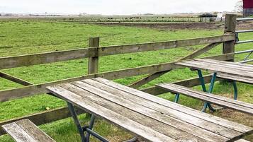 Una valla de madera y una mesa de picnic en un campo cubierto de hierba, con vacas al fondo.