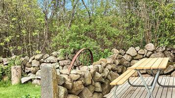 A stone wall with a wooden bench and a metal table, surrounded by greenery and trees.