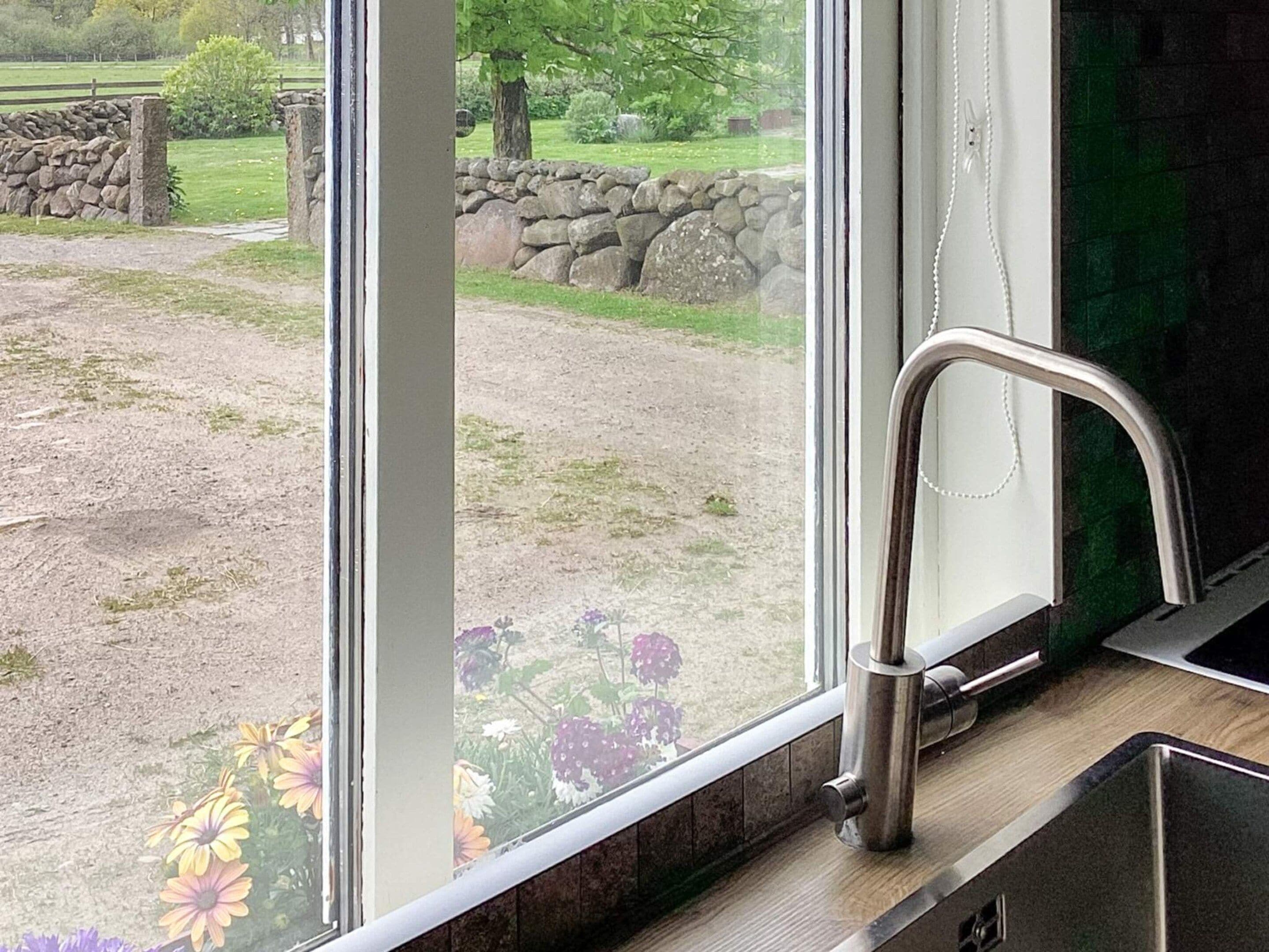 A kitchen with a stainless steel faucet and a view of a garden through a large window.
