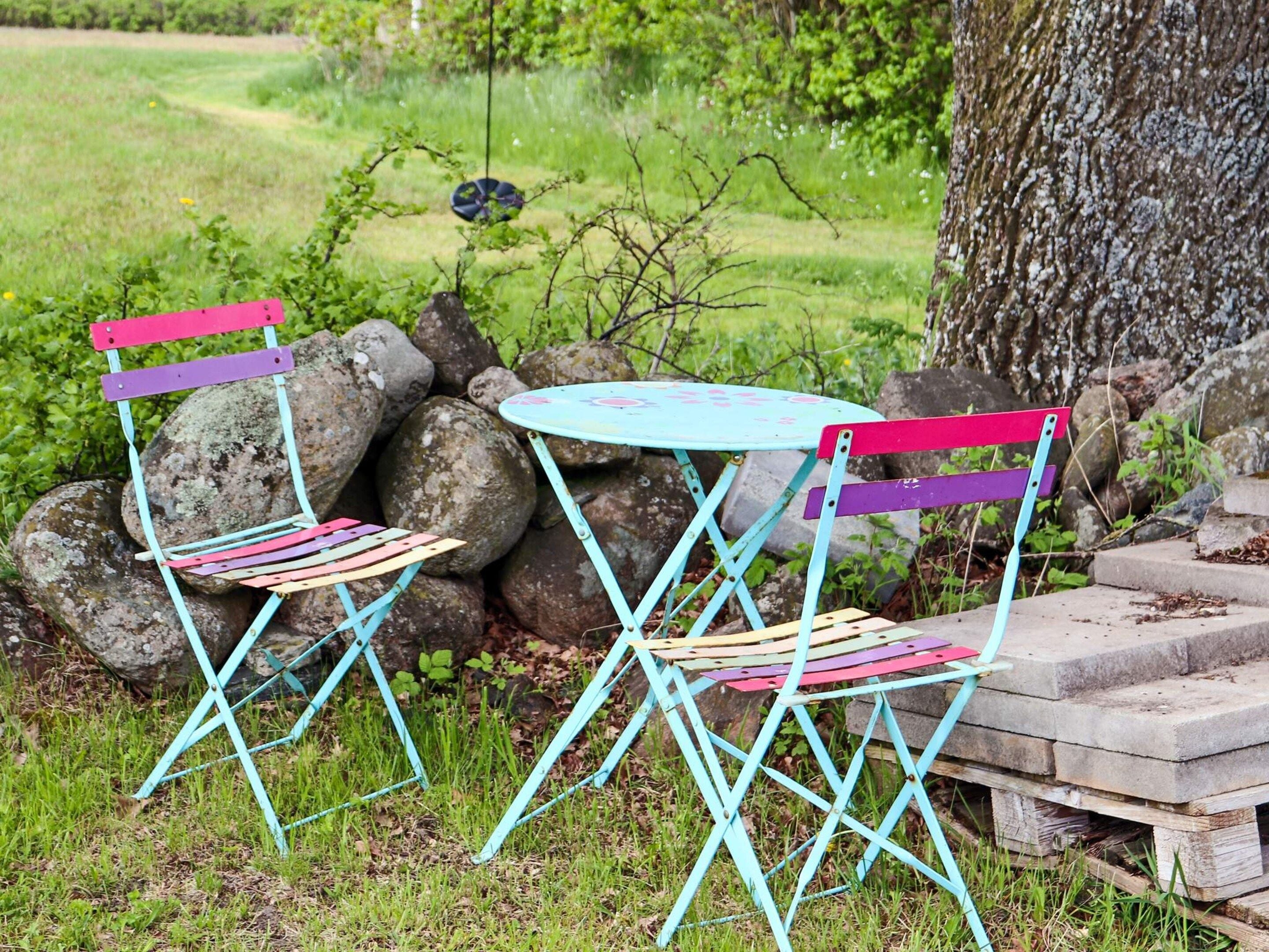 Dos sillas exteriores con una mesa, frente a un fondo de rocas y vegetación.