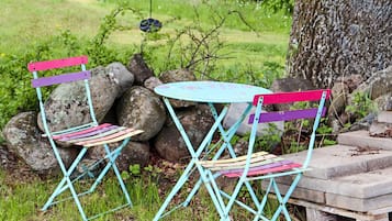 Dos sillas exteriores con una mesa, frente a un fondo de rocas y vegetación.