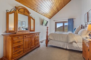 Ein Schlafzimmer mit einem hölzernen Schminktisch, einem Bett mit weißer Bettwäsche, einem großen Spiegel und einem an der Wand befestigten Fernseher.