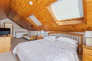 Ein Schlafzimmer mit einem großen Bett, einem Holzkopfteil, Nachttischen, einem Fernseher und einem Oberlicht.