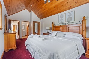 Ein Schlafzimmer mit Holzboden, einem großen Bett mit weißer Bettwäsche, einem Nachttisch aus Holz und einem Spiegel an der Wand.
