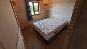 Ein Zimmer mit Holzwänden, einem Bett, einem Fenster mit Vorhängen und einer Wandleuchte.