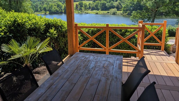 Eine Holzterrasse mit Tisch und Stühlen, mit Blick auf einen See und bewaldete Hügel.