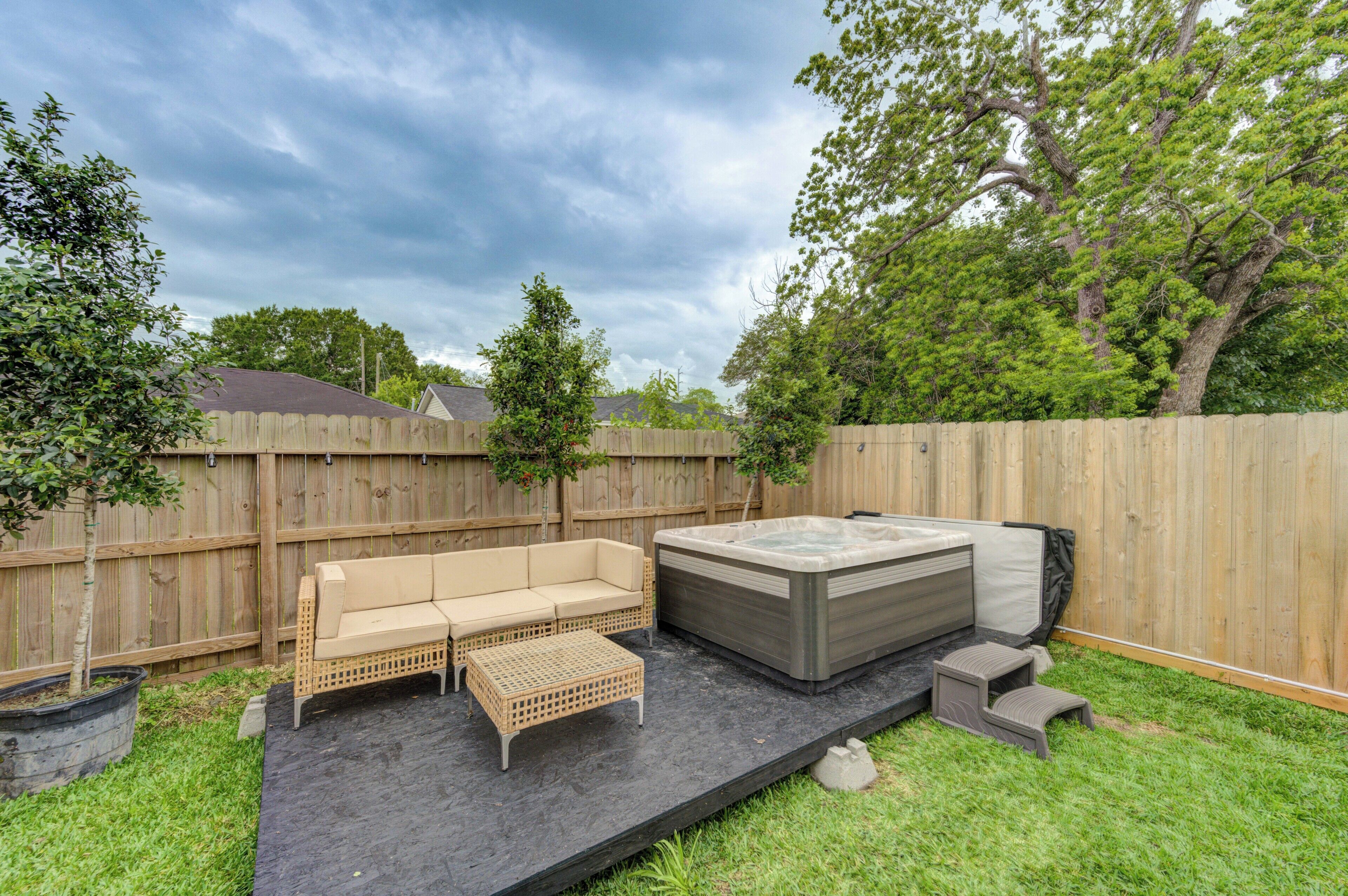 A backyard with a wooden fence, a beige sofa, a hot tub, and a small table.