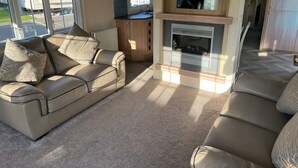 A living room with a sofa, a fireplace, and a view of the outside. - 261 @ Owens Caravan Park (Abergele)