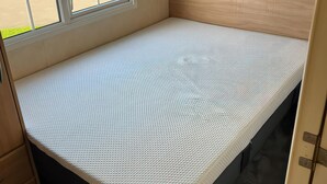 A small, single-bed room with a white mattress, wooden headboard, and a window. - 261 @ Owens Caravan Park (Abergele)