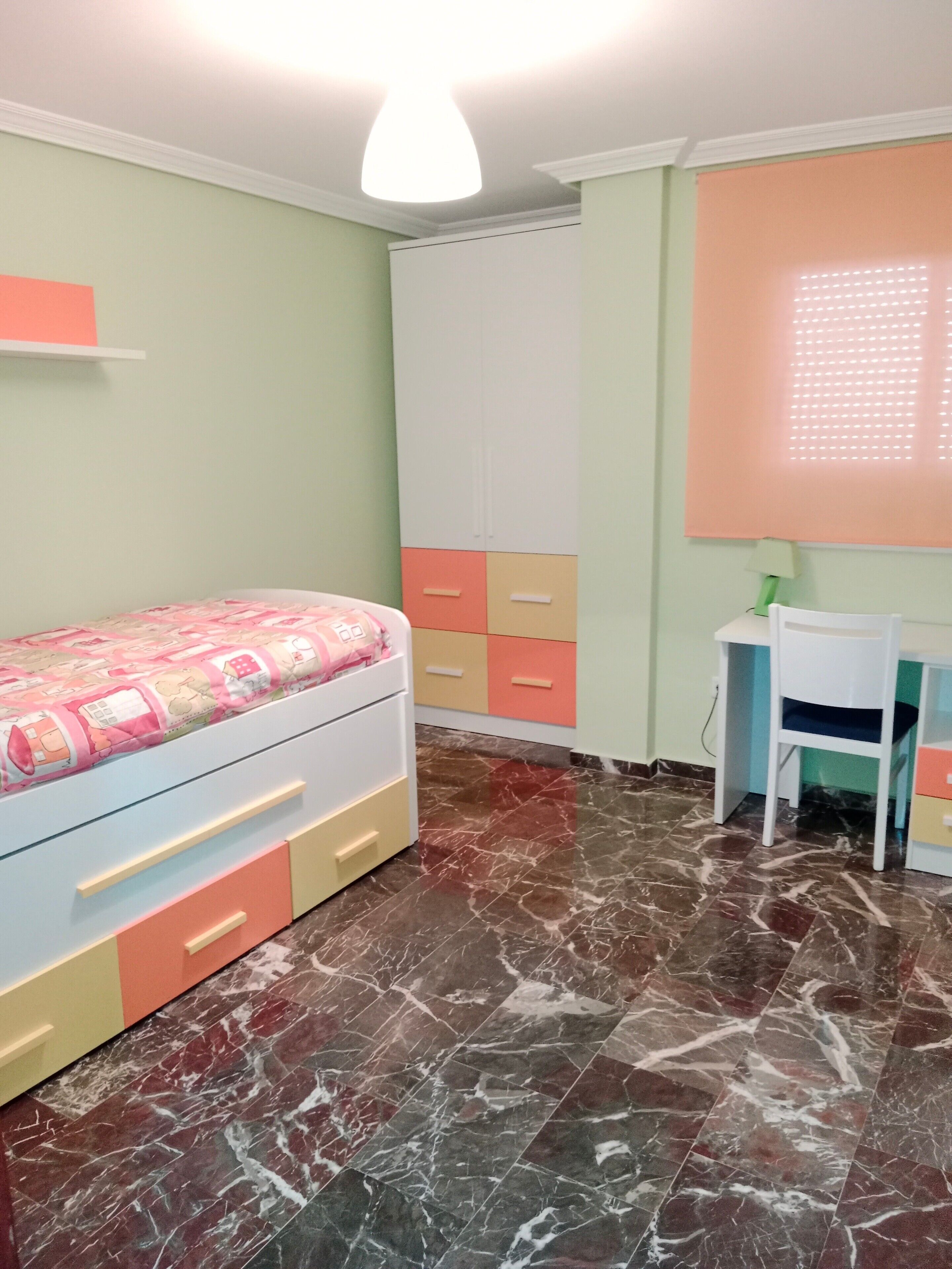 A bedroom with a bed, a desk, and a wardrobe.