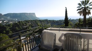 A balcony with two chairs, a railing, and a view of a coastal landscape with trees and a mountain in the distance. - T3 exceptional sea view with large equipped terrace (Cassis)