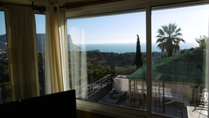 A room with a large window overlooking a scenic landscape with trees and a view of the sea. - T3 exceptional sea view with large equipped terrace (Cassis)