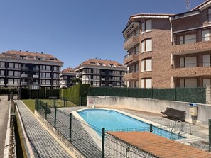 A swimming pool surrounded by a fence, with a bench and a trash bin nearby. - Apartment Bajosaltos 6905 (Noja)