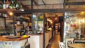 A restaurant interior with a bar area, seating, and a kitchen visible through a glass partition.