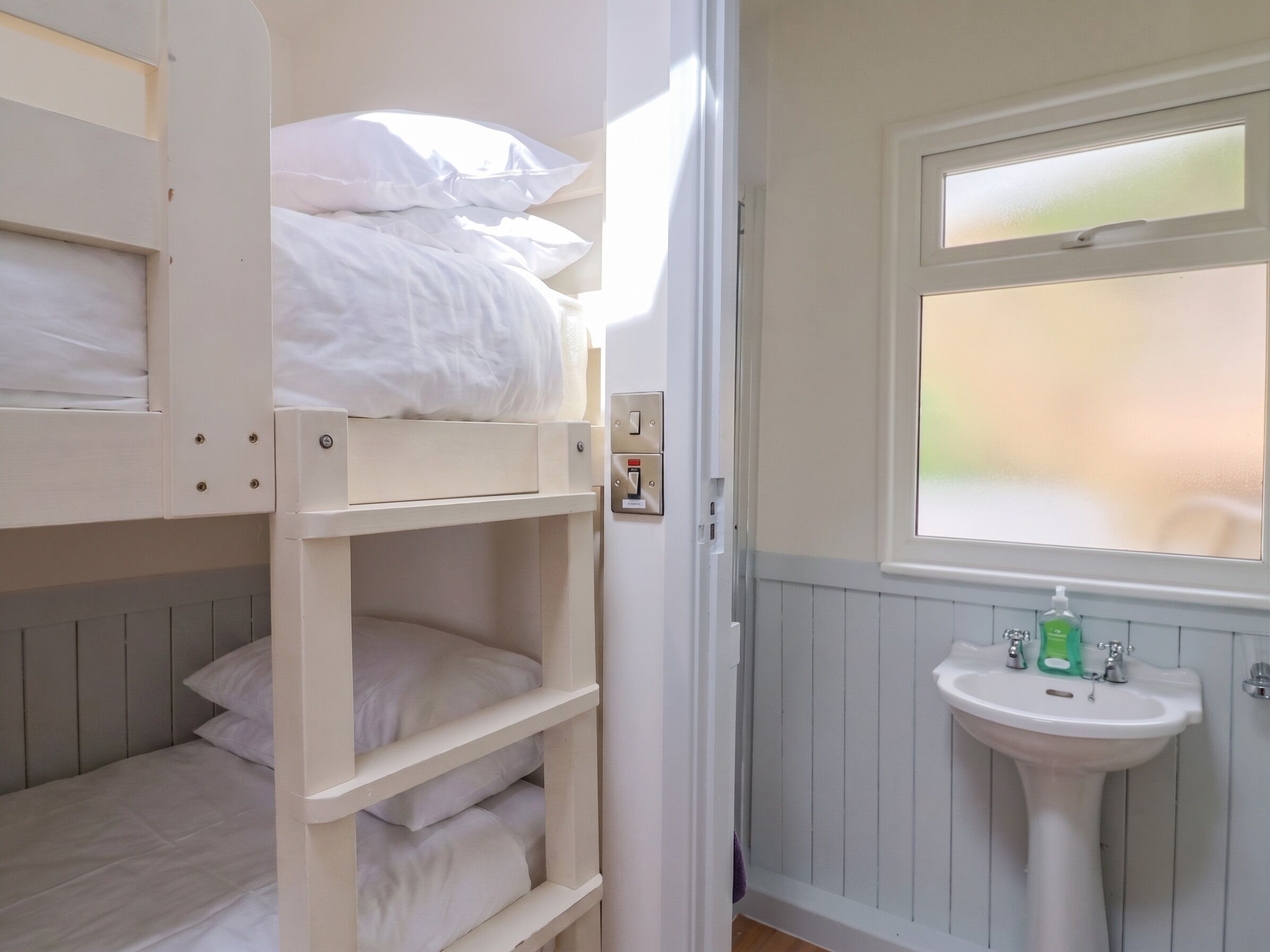 A bunk bed with white bedding, a white sink with green soap, and a window with a view.