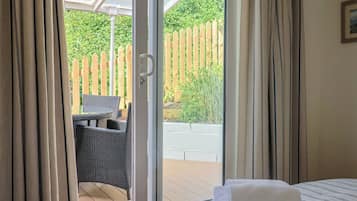 Quarto com cama, janela com cortinas e vista para uma cerca de madeira e vegetação lá fora.