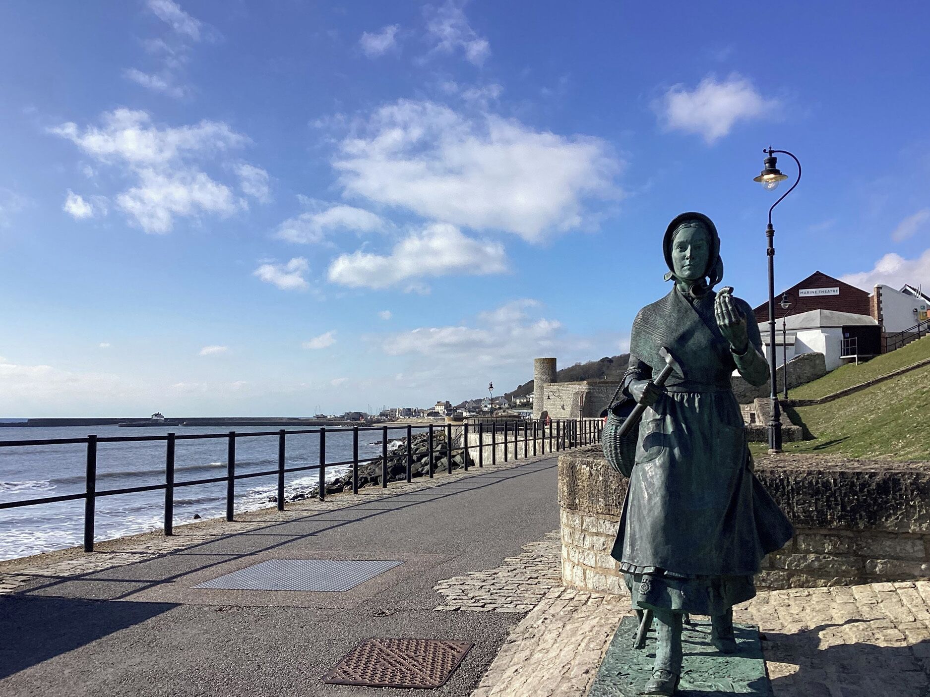A coastal walkway with a statue, a stone wall, and a view of the sea.
