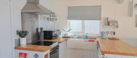 A compact kitchen with a stove, microwave, and sink, wooden countertops, and a window with blinds.