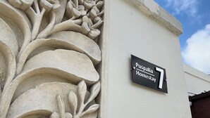 Una esquina de edificio con una escultura de piedra floral y un letrero negro que dice 'Puspaku Homesstay 7'.