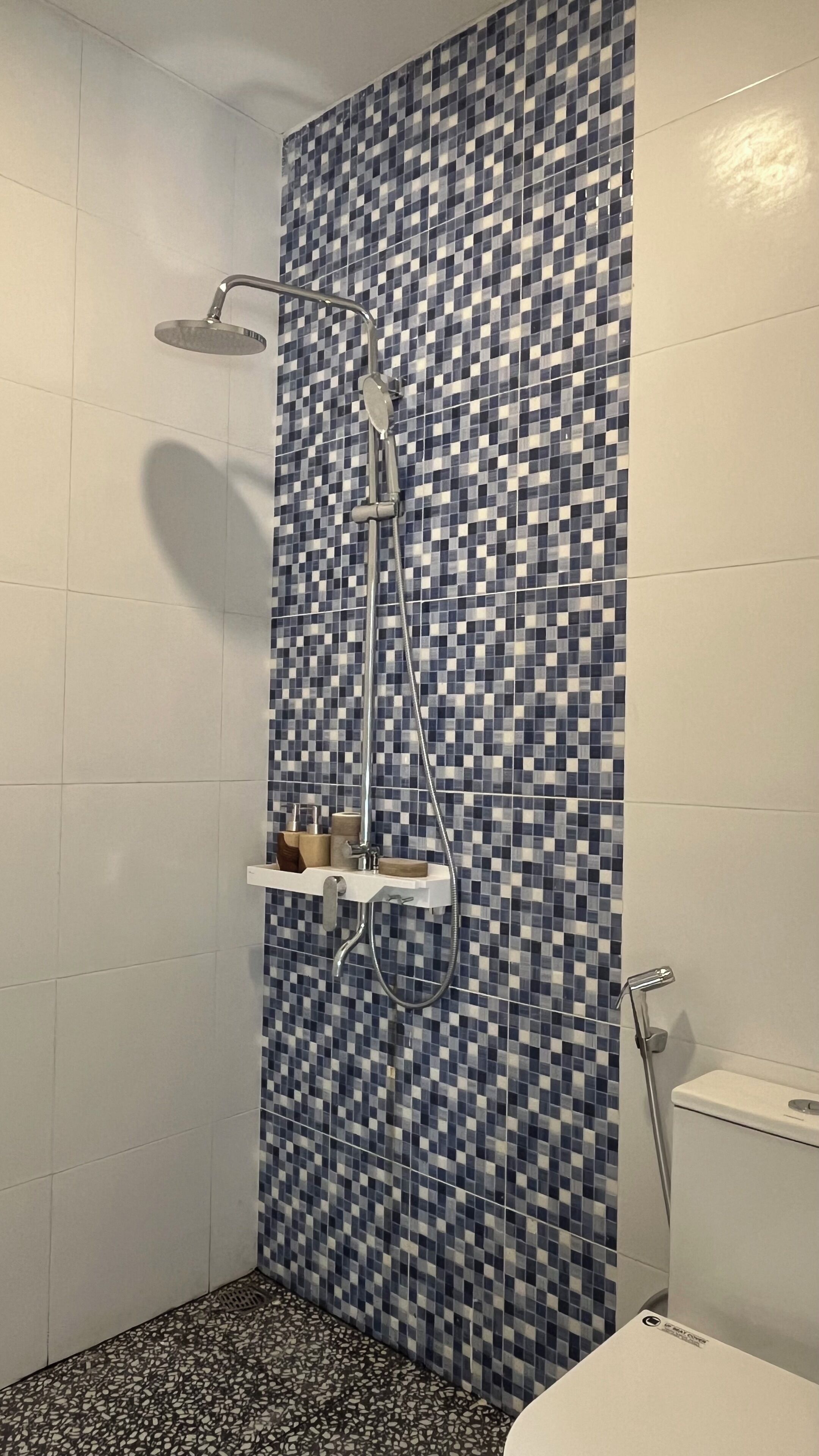 Eine Dusche mit Kachelwand in Schachbrettmuster, einer Handbrause und einem wandmontierten Wasserhahn.