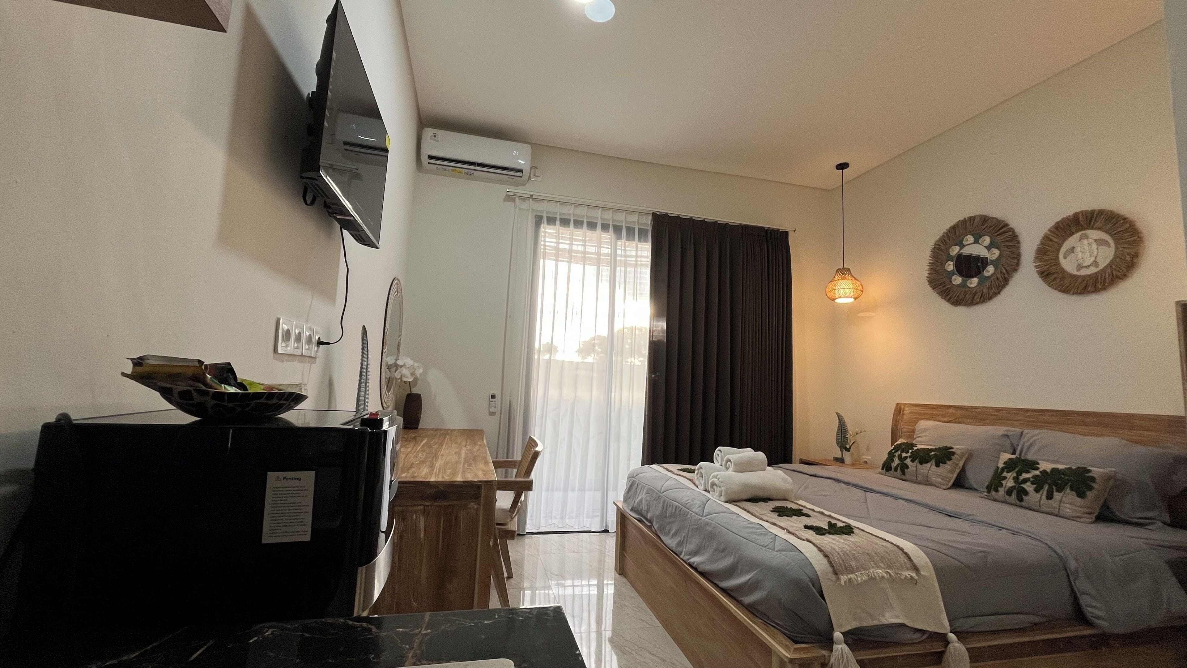 A hotel room with a bed, a desk, a TV, an air conditioner, and a window with curtains.