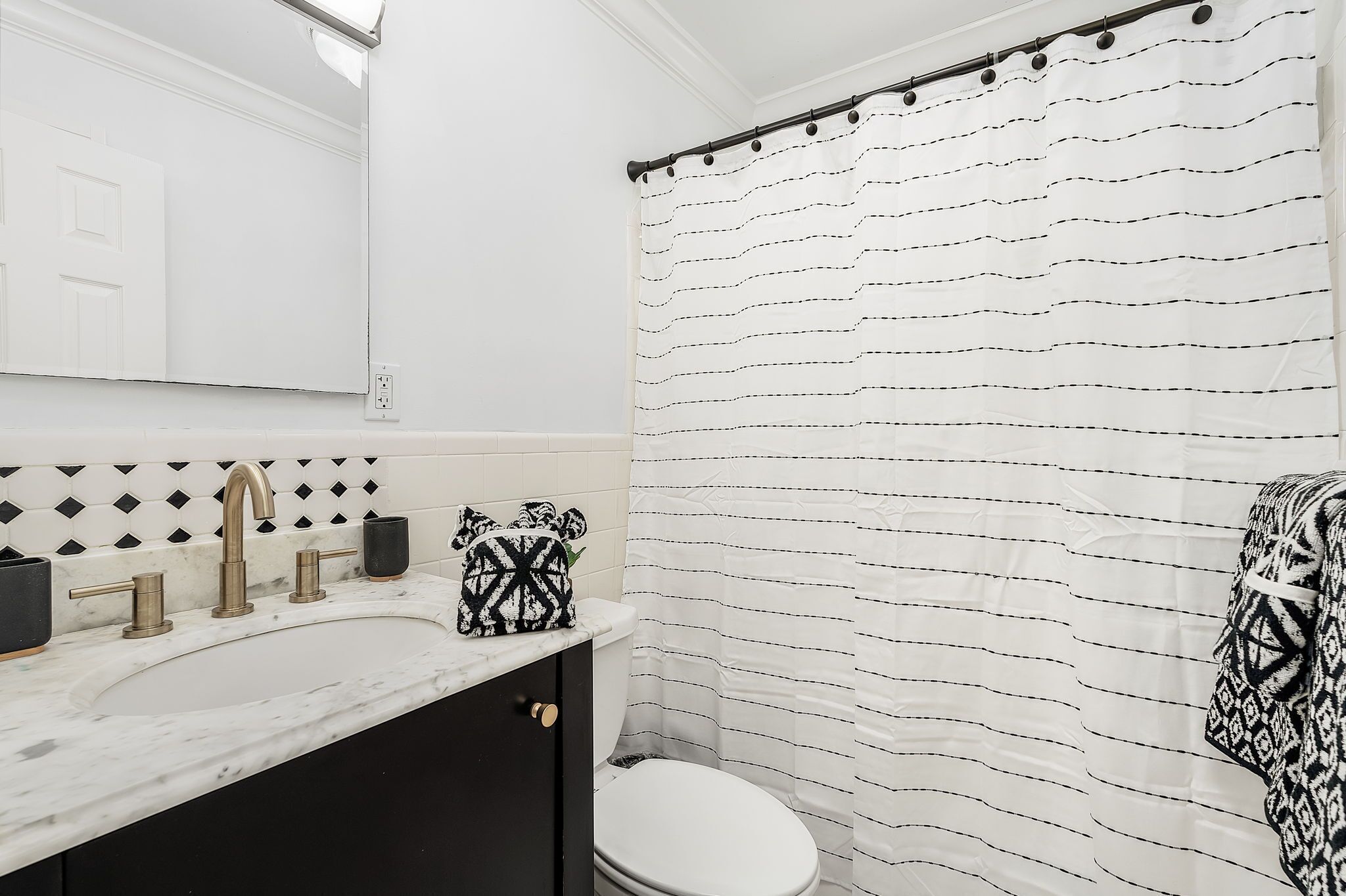 Une salle de bain avec un lavabo blanc, un rideau de douche à rayures noires et blanches et des toilettes blanches.