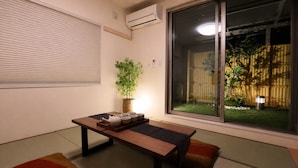 A room with tatami mats, a low table with a tea set, a potted plant, and a sliding door to a garden. - Spacious 1,500 sq ft Japanese Bath House with 7 Bedrooms (Osaka City)