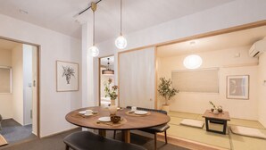 A modern dining area with a round table, benches, and a small side table with a plant. - Spacious 1,500 sq ft Japanese Bath House with 7 Bedrooms (Osaka City)