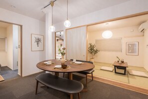Un espace repas moderne avec une table ronde, des bancs et une petite table d’appoint agrémentée d’une plante.