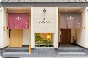 A hotel entrance with a sign reading 'ASUKA' and two doors, one with a wooden facade and the other with a beige facade. - Spacious 1,500 sq ft Japanese Bath House with 7 Bedrooms (Osaka City)