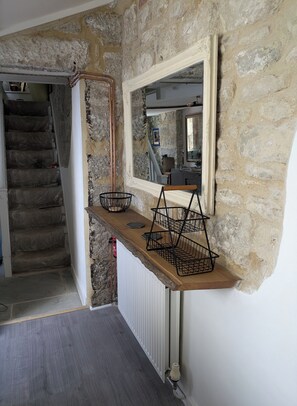 A staircase with a stone wall, a wooden shelf with baskets, and a mirror. - Newly Renovated  Fisherman’s Cottage with Large Courtyard • Near Chesil Beach (PORTLAND)